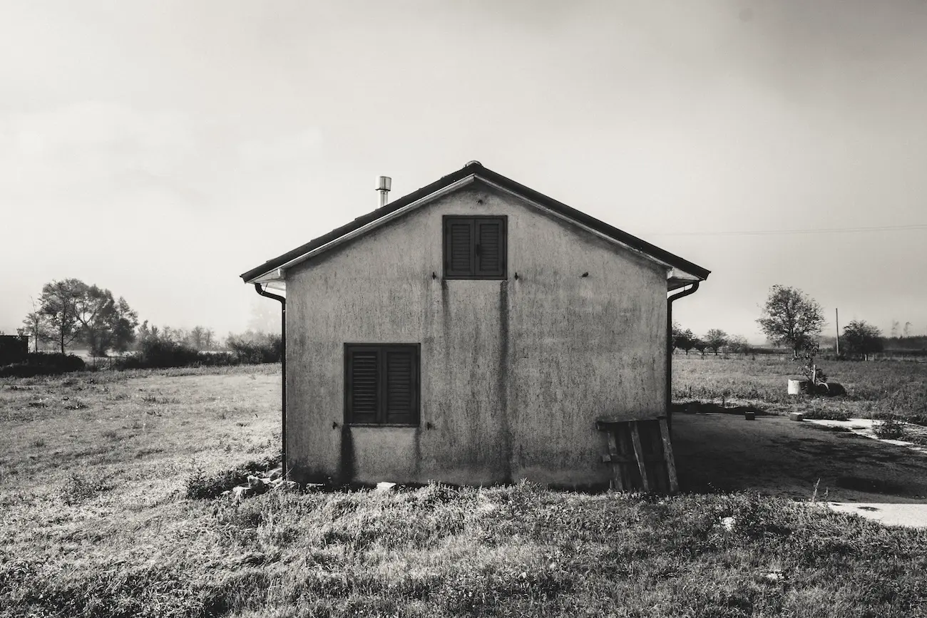 Casetta isolata ai margini di un campo erboso, cielo lattiginoso. Irpinia: architettura del silenzio e quiete rurale.