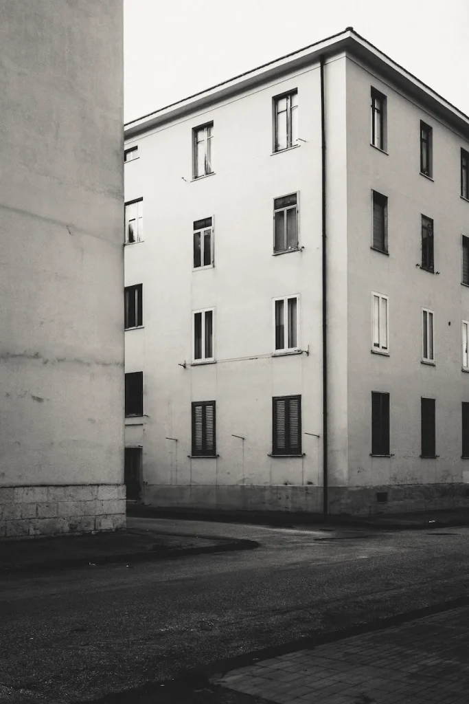 Angolo di edificio residenziale con finestre chiuse e strada vuota in primo piano.