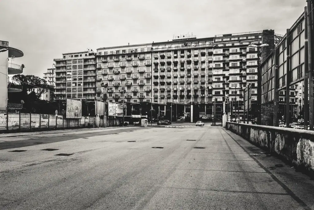 Grande area asfaltata tra palazzi residenziali, con prospettiva aperta e atmosfera sospesa.