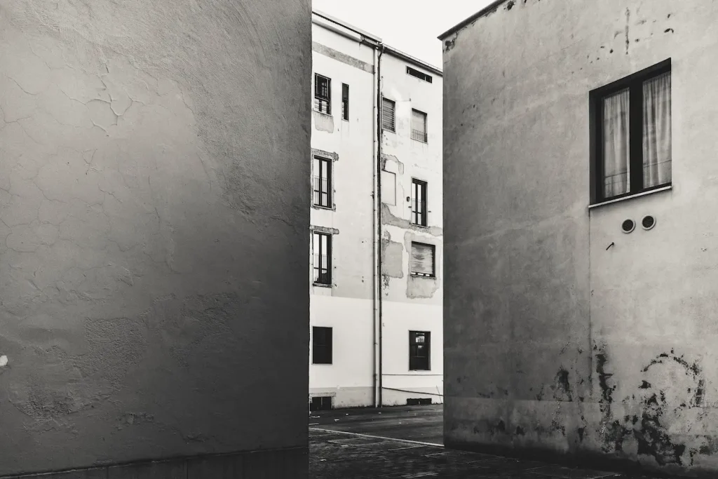 Passaggio stretto tra pareti nude e palazzi chiari, con superfici segnate dal tempo.