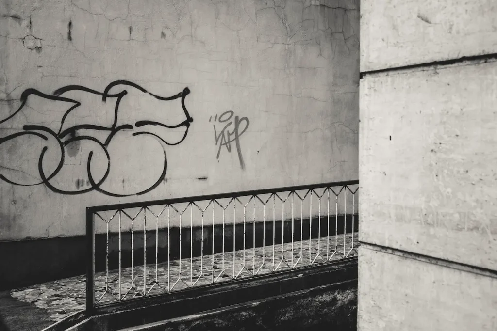 Graffiti, ringhiera e pareti ravvicinate compongono un frammento urbano laterale.